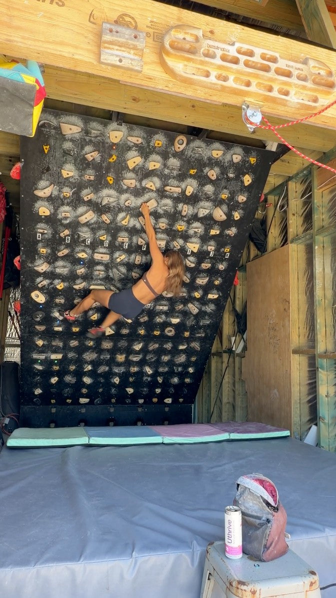 Brooklyn bouldering on her home climbing wall with a can of Uthrive on the stool